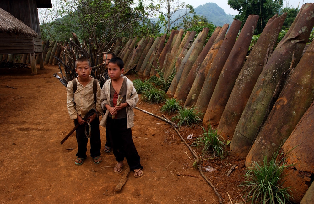 Laos: children play next to a wall of unexploded bombs